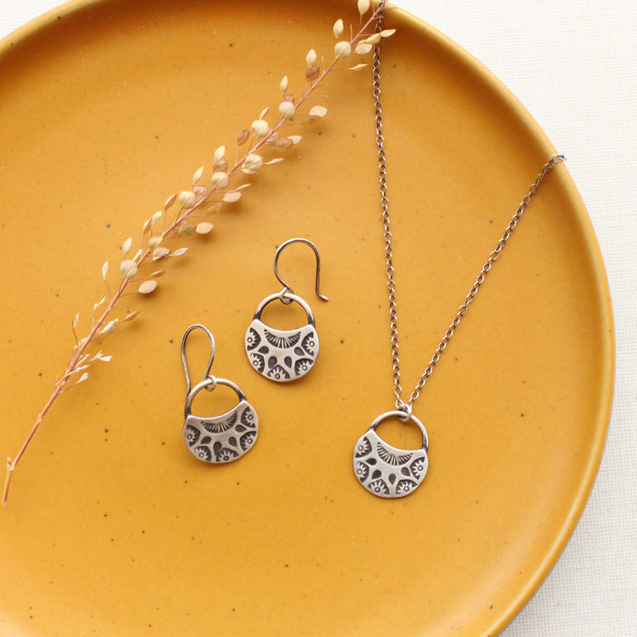 The midnight bloom necklace and earrings styled on a yellow plate with dried grass