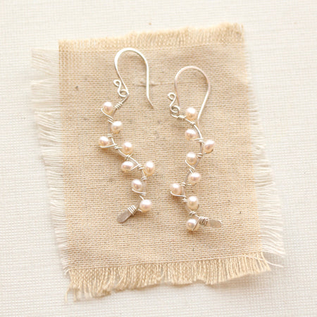 The elegant pearl wrapped silver vine earrings styled on tan linen