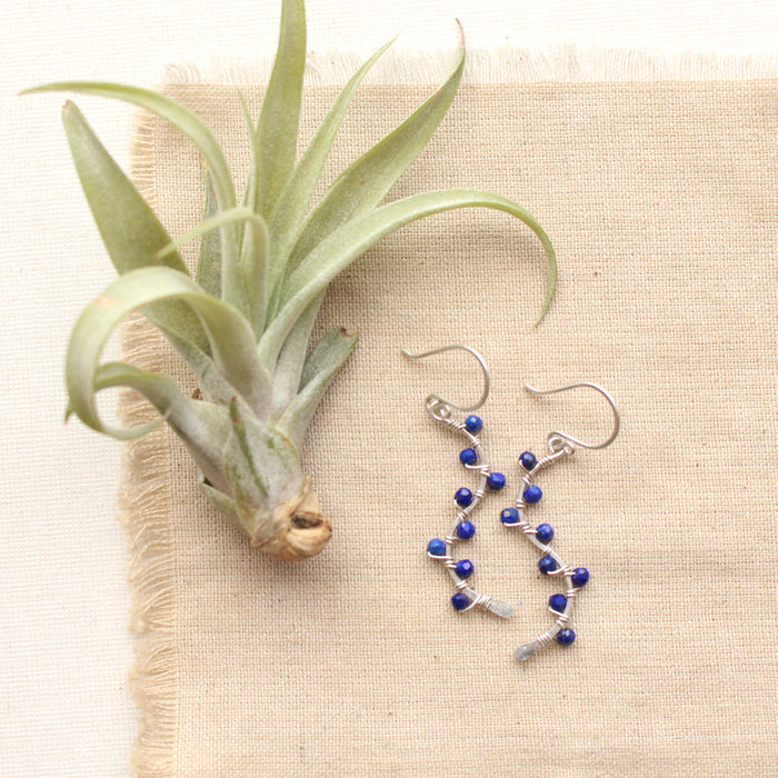 The colorful lapis wrapped silver vine earrings styled on tan linen with an airplant