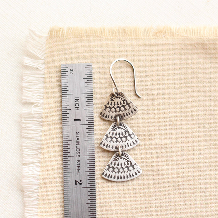 An asmi trio triangle earring next to a ruler for size reference