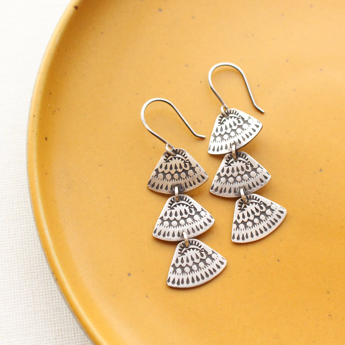 The asmi trio triangle long earrings styled on a yellow plate