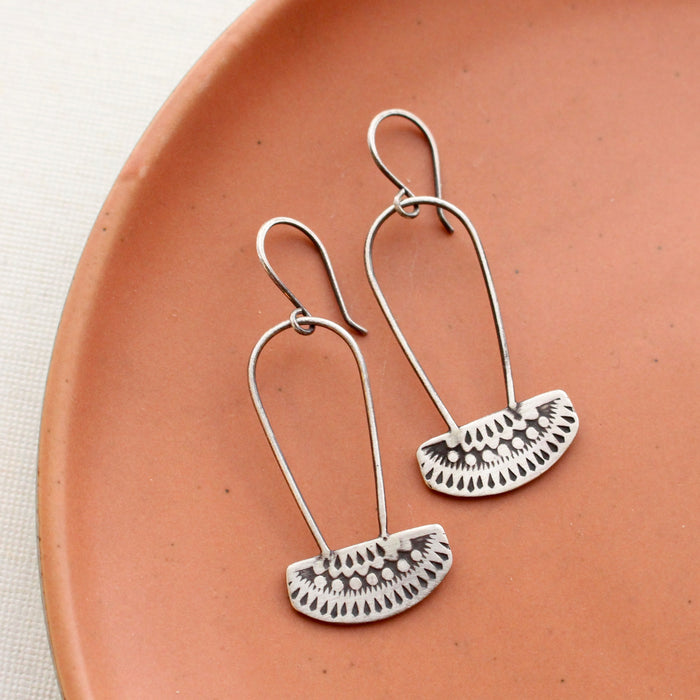 The asmi silver long loop earrings styled on a red plate