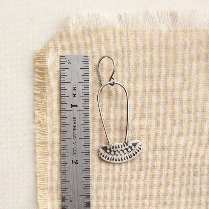 An asmi long loop earring next to a ruler for size reference