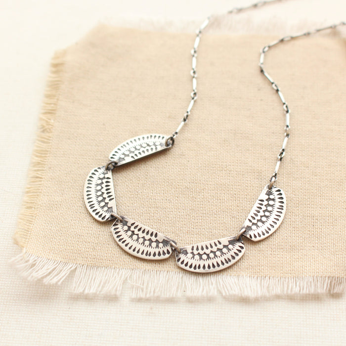 A close up shot of the asmi 5 collar necklace styled on tan linen