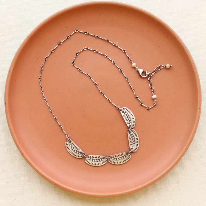 The asmi 5 collar necklace styled on a red plate to show the adjustable clasp chain