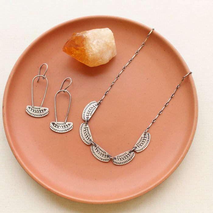 The asmi long loop earrings and asmi collar necklace styled on a red plate with a crystal