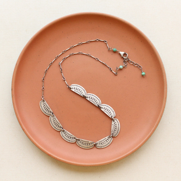 The asmi full collar necklace styled on a red plate to show the adjustable chain closure