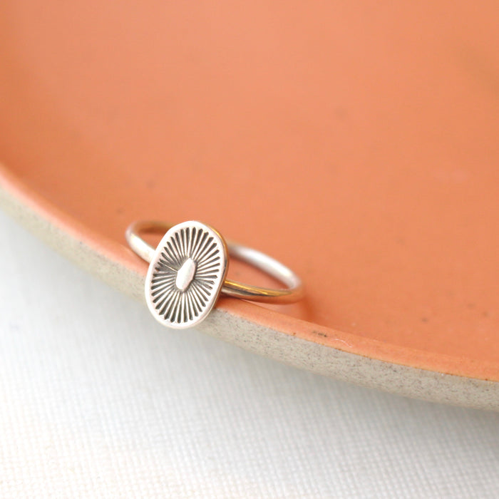 Stamped silver ring with burst design styled on a red plate