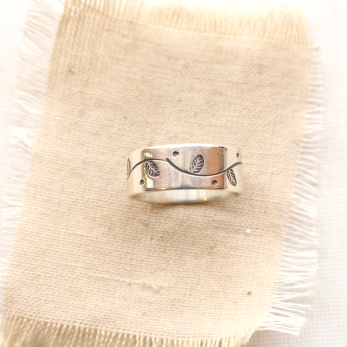 The stamped leaf garland silver band ring styled on tan linen