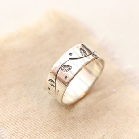 The stamped leaf garland wide band ring styled on tan linen