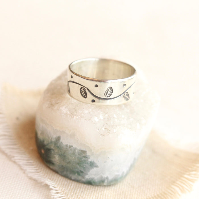 The stamped leaf garland silver band ring styled on a crystal and tan linen