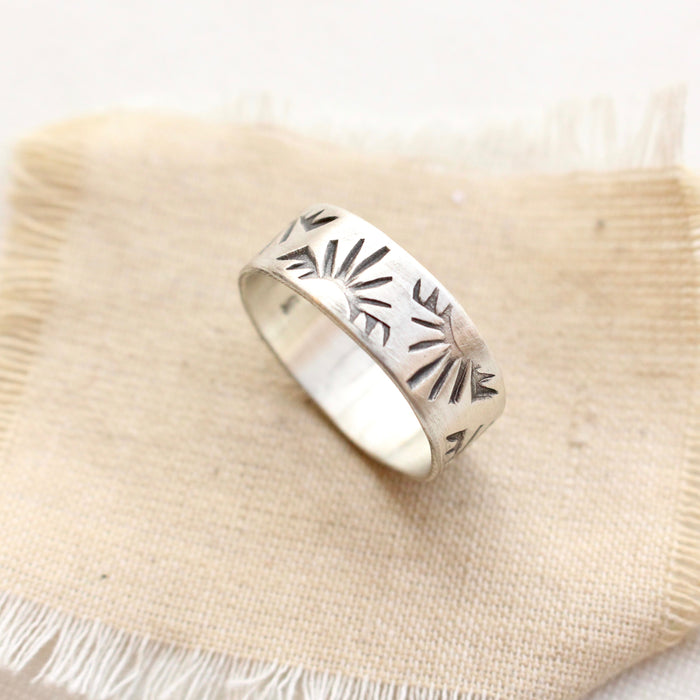 The stamped sun rise silver band ring is styled on tan linen