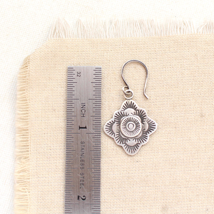 A talara winter sun earring next to a ruler for size reference