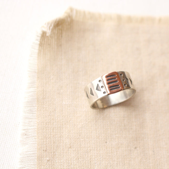 The rustic stamped bronze and silver ring styled on tan linen