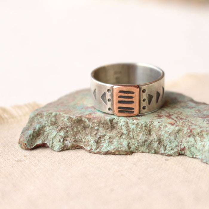 The southwest stamped bronze and silver band ring styled on a stone and tan linen