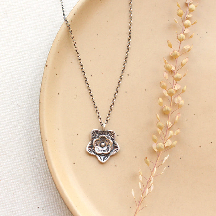 The layered cactus flower silver dot necklace styled on a tan plate with dried grass