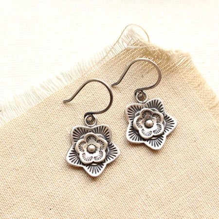 The silver layered cactus flower earrings styled on tan linen