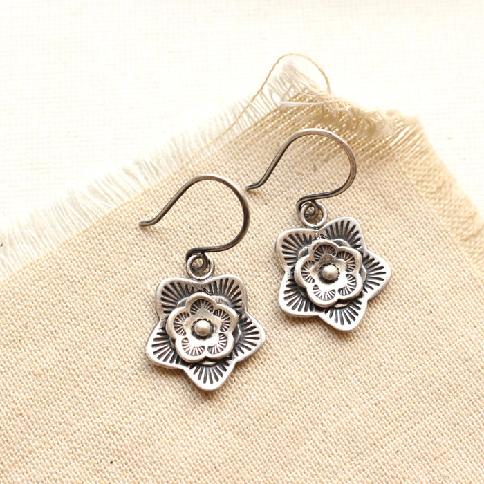 The silver layered cactus flower earrings styled on tan linen