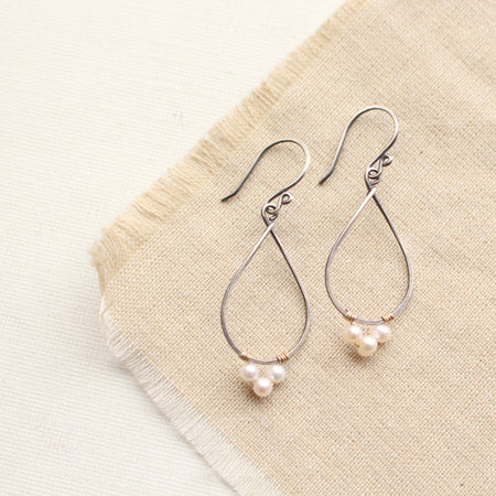 The elegant pearl wrapped teardrop mixed metal hoop earrings styled on tan linen