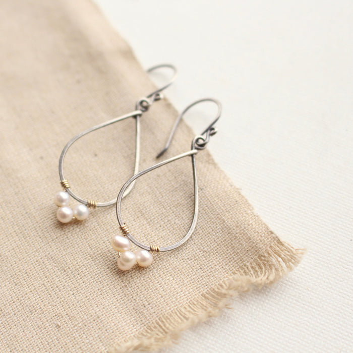 The elegant pearl wrapped teardrop mixed metal hoop earrings styled on tan linen