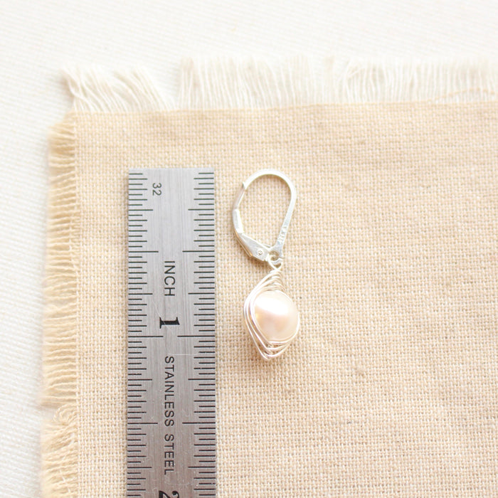 A silver wrapped perfect pearl earring next to a ruler for size reference