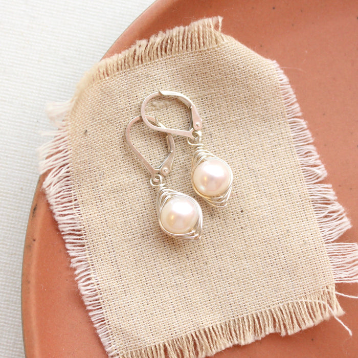 The silver wrapped perfect pearl earrings styled on a red plate with linen