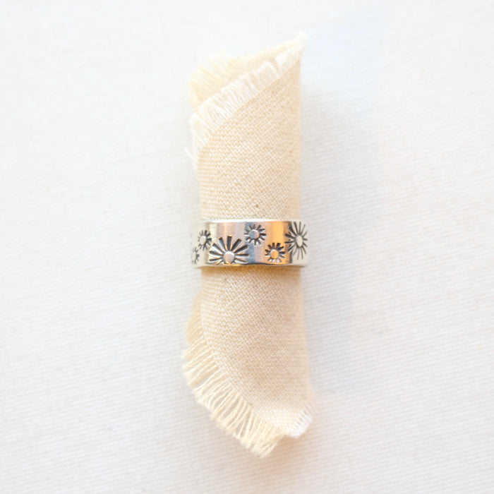 The sun stamped wide band ring styled on a roll of tan linen
