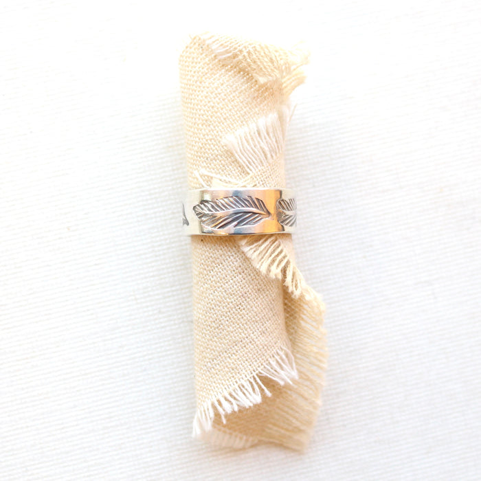 The stamped feather silver band ring styled on rolled tan linen