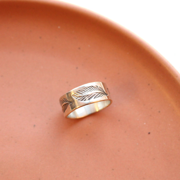 The stamped silver feather ring styled on a red ceramic plate