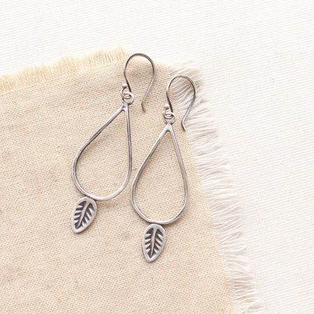 The leaf teardrop hoop earrings styled on tan linen