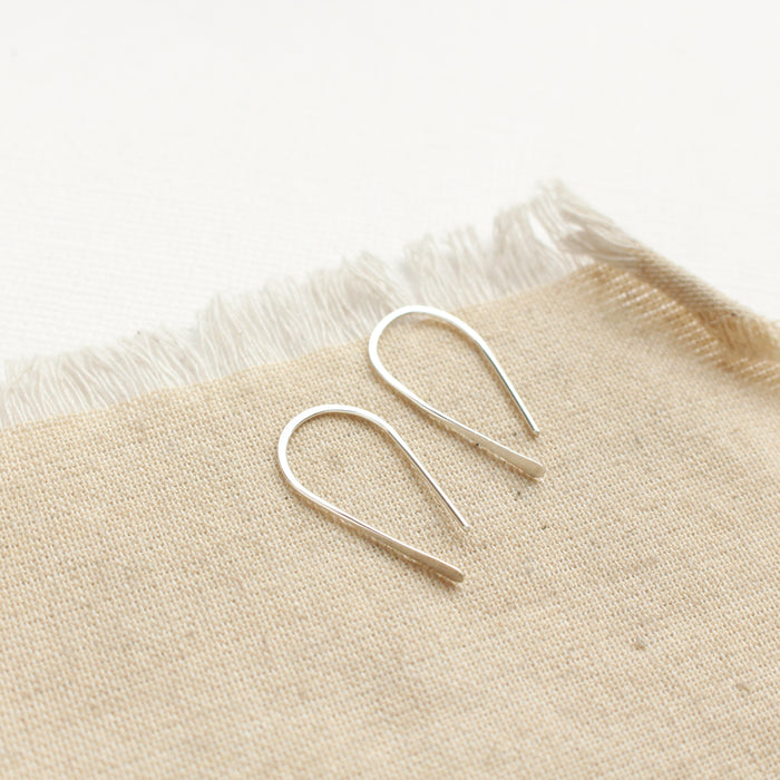The silver hook earrings styled on tan linen