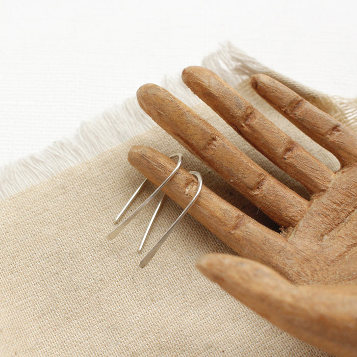 The silver hook earrings styled on a wooden hand and linen