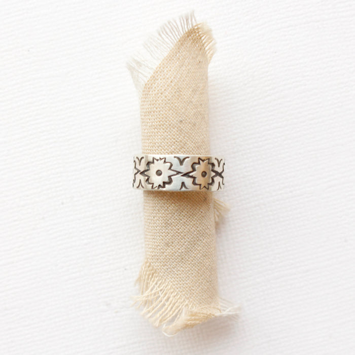 The stamped silver arabesque band ring styled on rolled tan linen