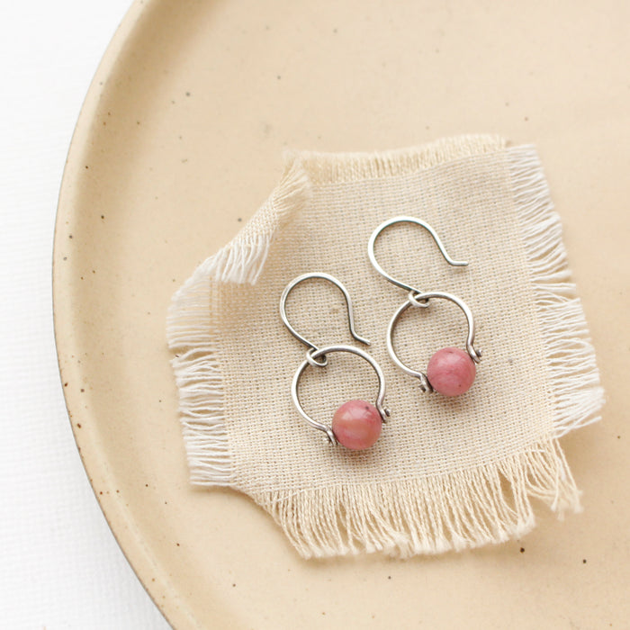 The rhodonite la cloche earrings styled on a tan plate with linen