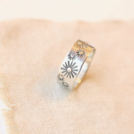 Hand stamped silver ring with small and large sun designs styled on tan linen.