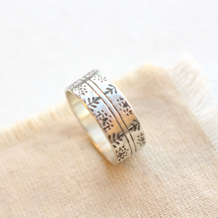 Silver band ring imprinted with delicate Nordic design styled on tan linen.