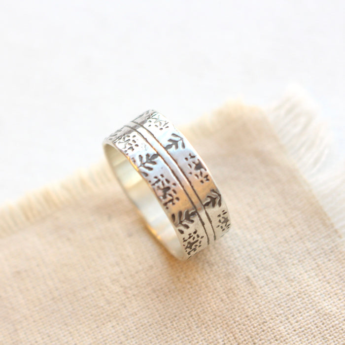 Silver band ring imprinted with delicate Nordic design styled on tan linen.