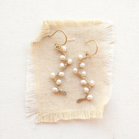Small white pearls wrapped on gold vines earrings styled on tan linen.
