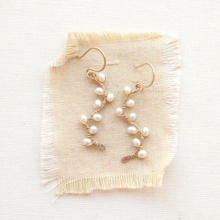Small white pearls wrapped on gold vines earrings styled on tan linen.