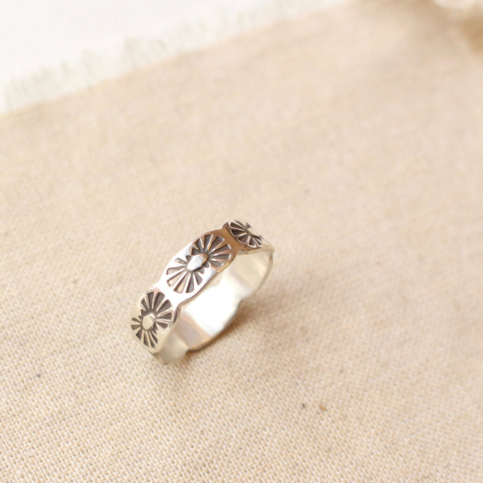 Stamped sun design on scalloped  edge silver ring styled on tan linen.