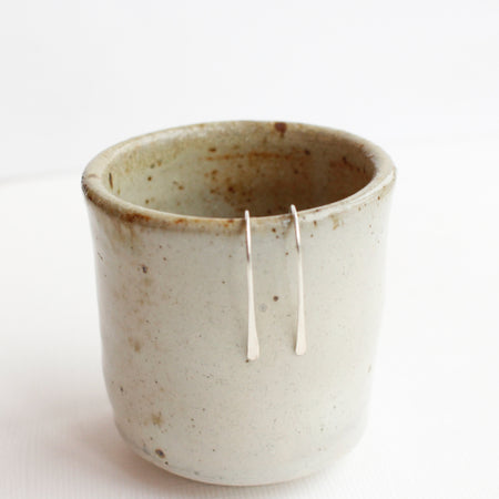 The silver hook earrings styled on a ceramic cup