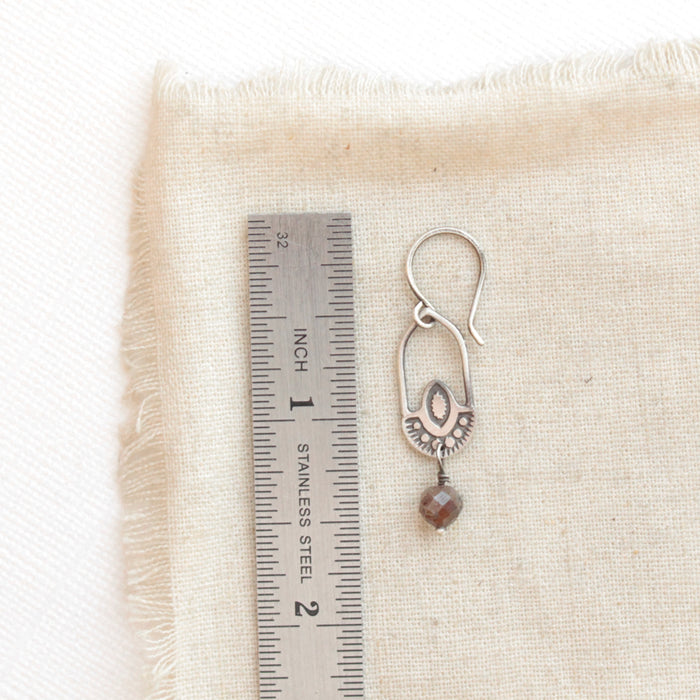 A brown zircon wanderer hoop earring next to a ruler for size reference