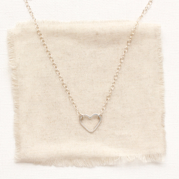 The floating silver heart necklace styled on tan linen
