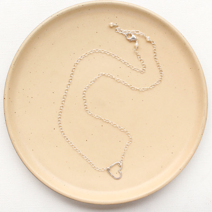 The floating silver heart necklace styled on a tan plate to show the adjustable lobster clasp closure