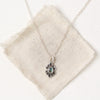 Sapphire gemstone in a stamped silver flower on silver chain on a cream colored canvas.