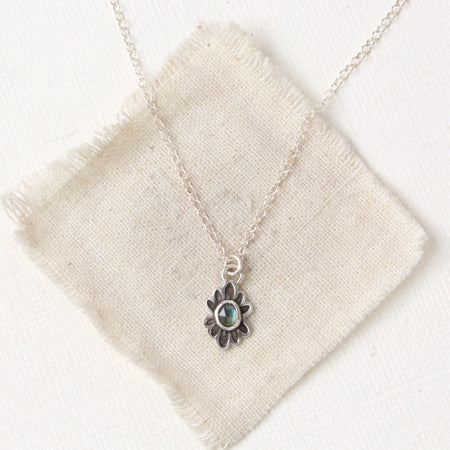 Sapphire gemstone in a stamped silver flower on silver chain on a cream colored canvas.