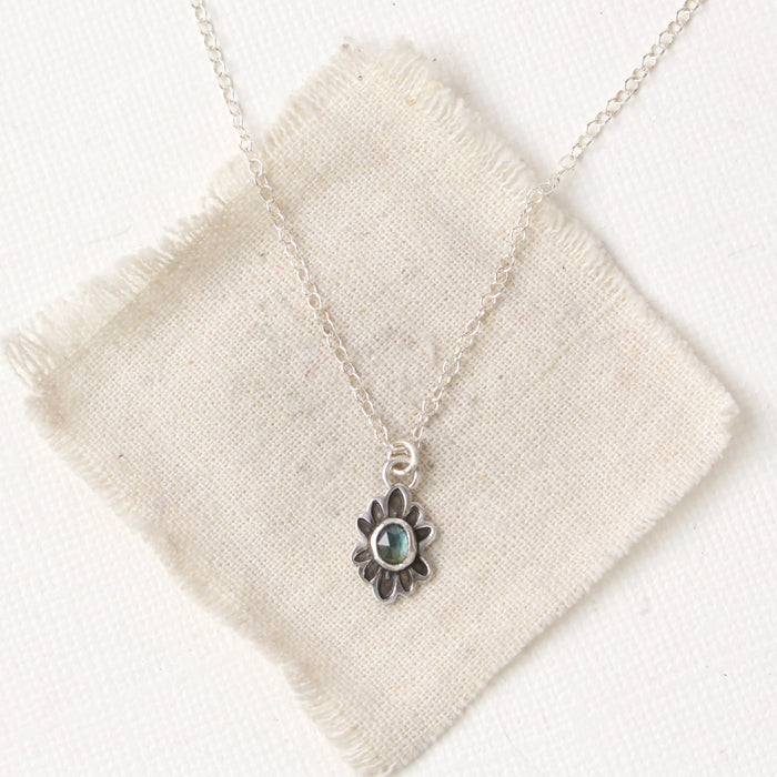 Sapphire gemstone in a stamped silver flower on silver chain on a cream colored canvas.