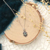 sapphire gemstone set in a stamped silver flower on silver chain on a piece of round wood with blue velvet 