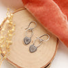 The layered heart earrings styled on wood with coral velvet and dried grass