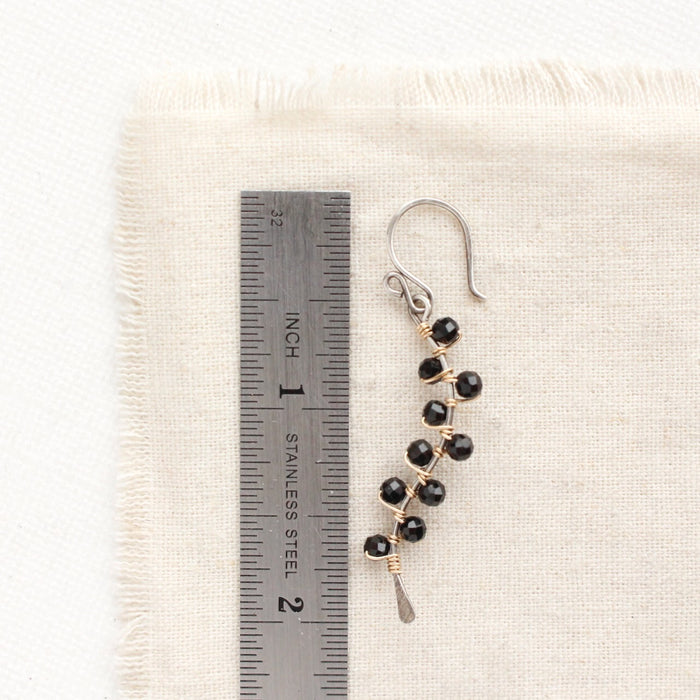 A black tourmaline vine earring next to a ruler for size reference